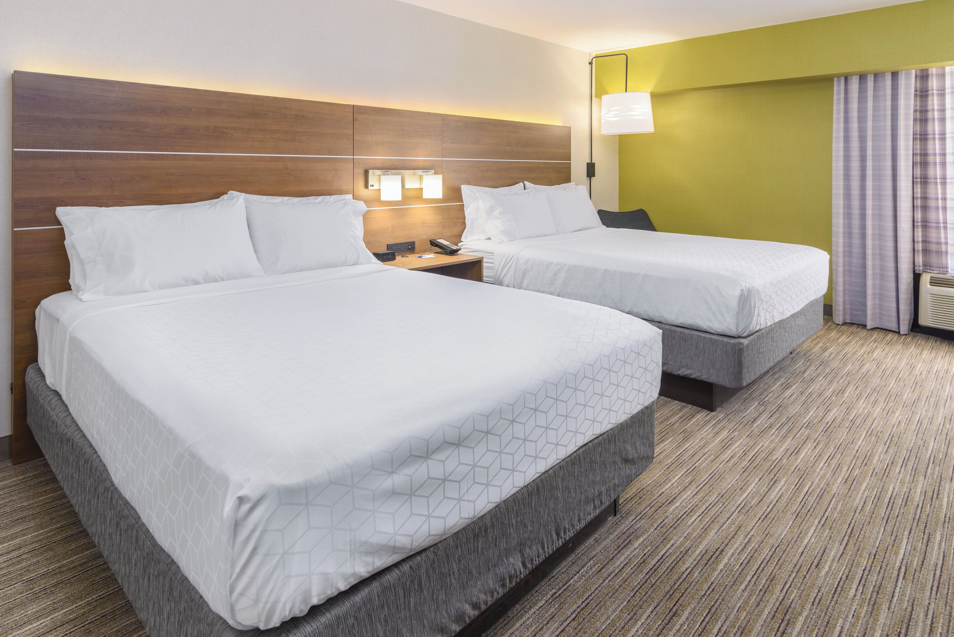 Habitación de hotel con dos camas, una mesita de noche, una lámpara y una ventana con cortinas.