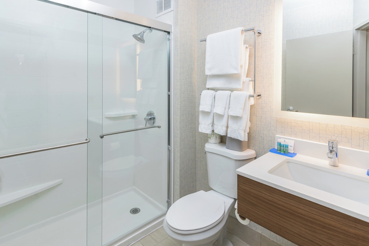A modern bathroom with a glass-enclosed shower, a white toilet, and a vanity with a mirror and sink.