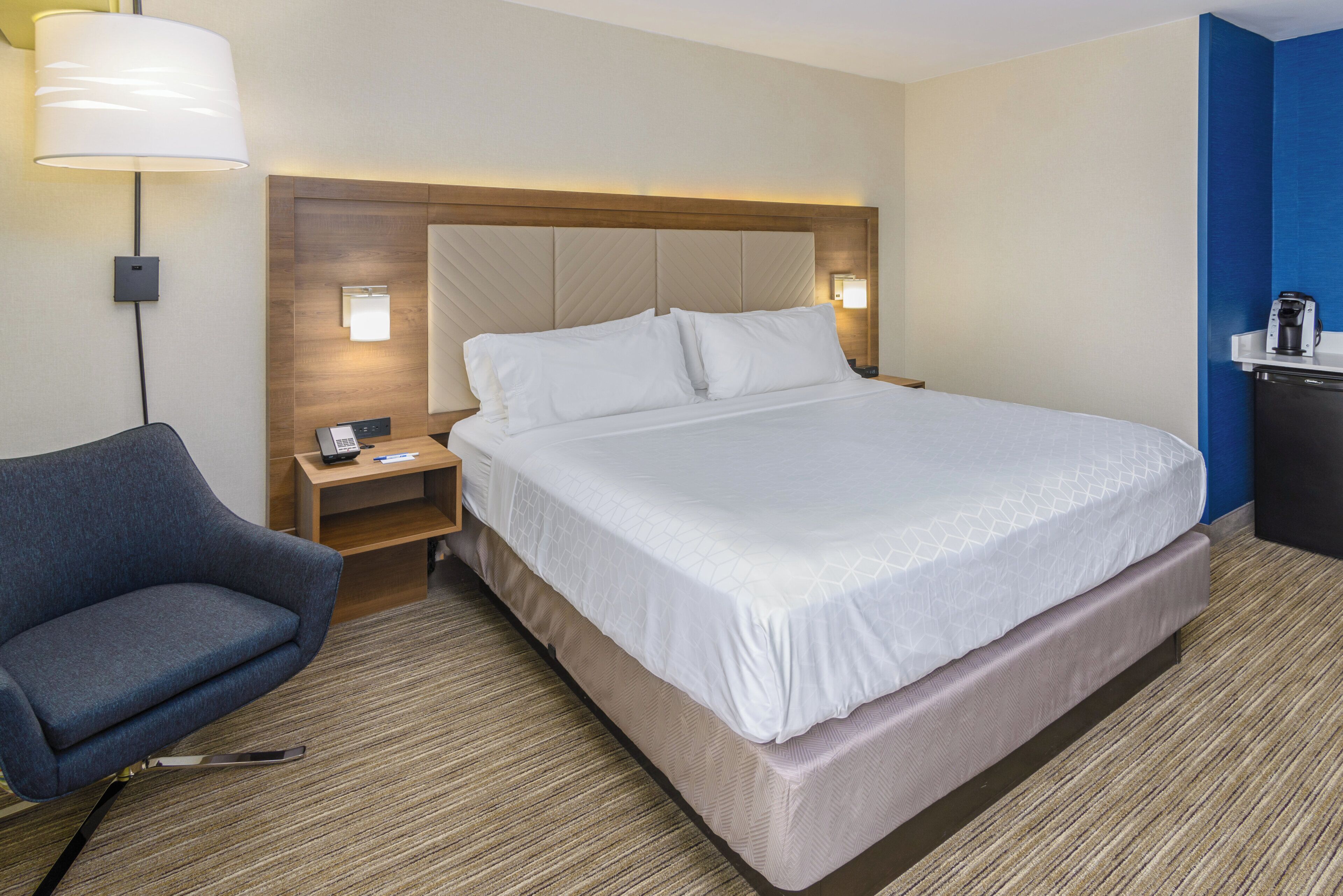 Une chambre d’hôtel équipée d’un lit, d’une chaise, d’une table de chevet, d’une lampe et d’une machine à café.