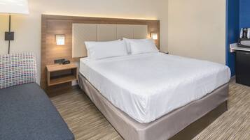 A hotel room with a large bed, a bedside table, a lamp, and a small desk with a coffee maker.