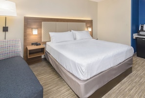 A hotel room with a large bed, a bedside table, a lamp, and a small desk with a coffee maker.