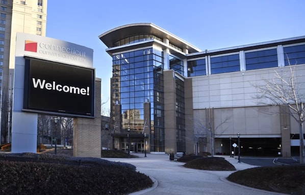 A modern building with a large digital welcome sign, a convention center sign, and a parking garage entrance.