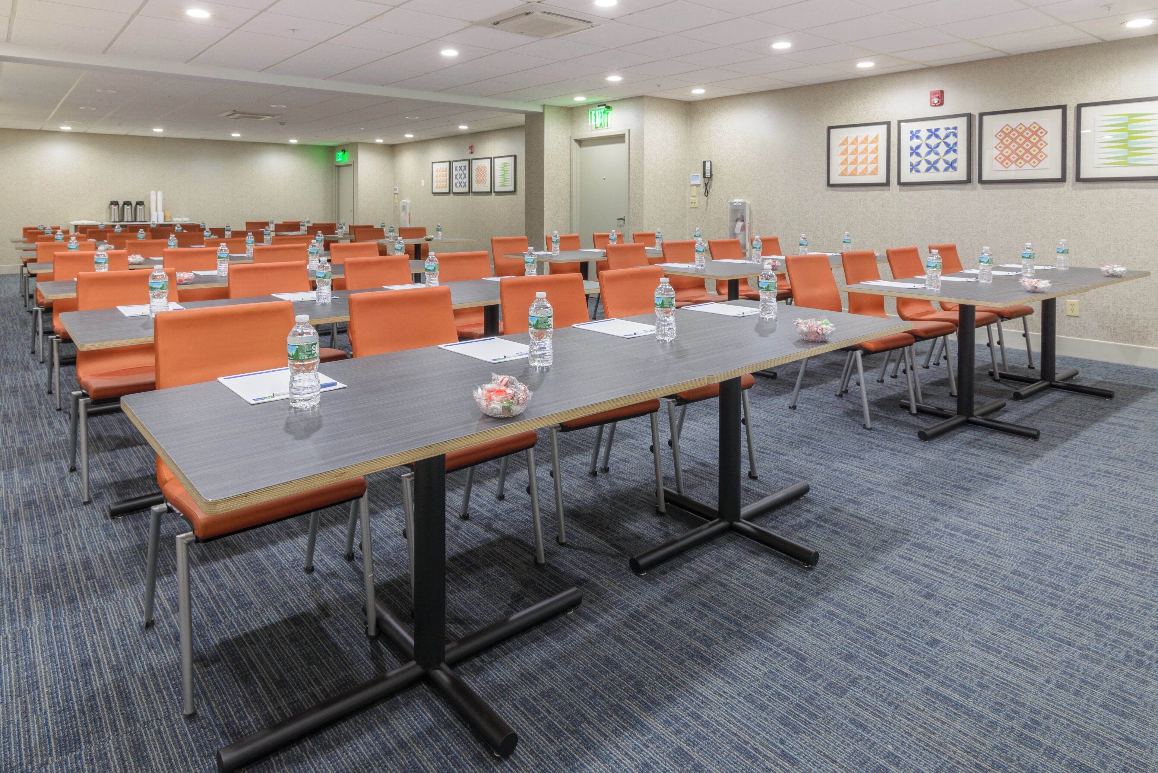 A conference room with multiple tables and chairs, equipped with water bottles and notepads.