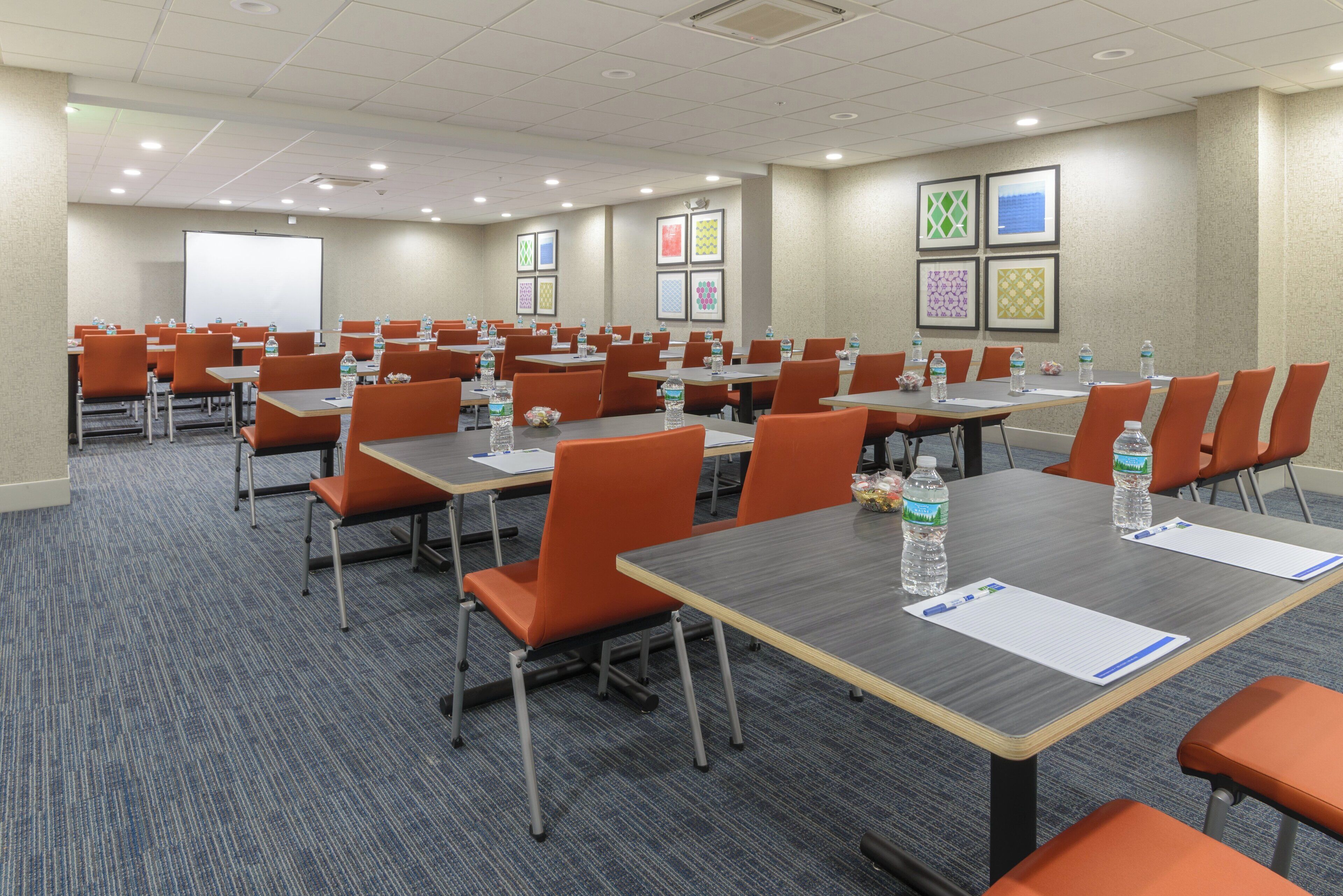 A conference room with multiple tables and chairs, equipped with water bottles and papers.