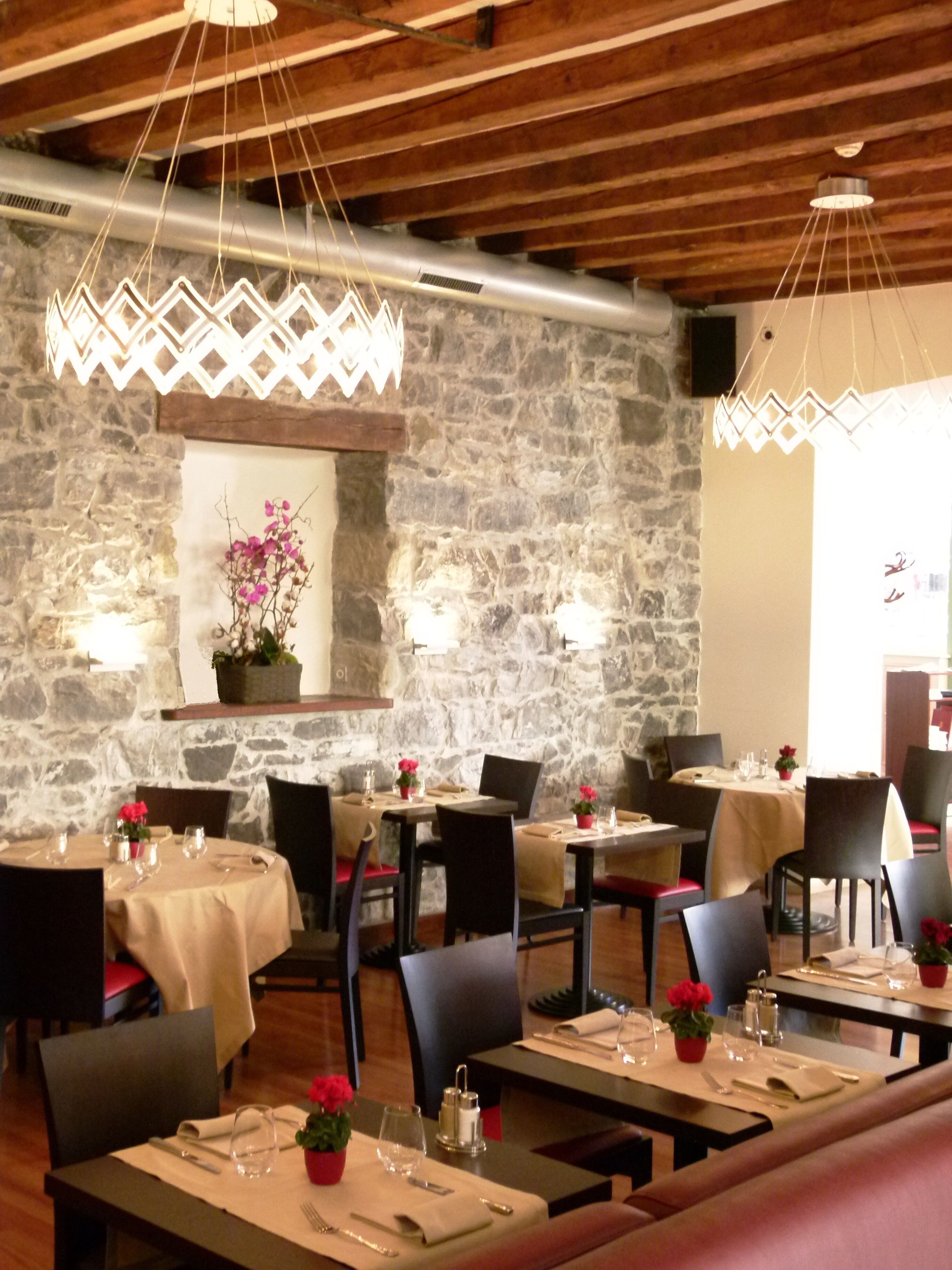Ein Restaurant mit Steinwänden, Holzbalken und gedeckten Tischen.