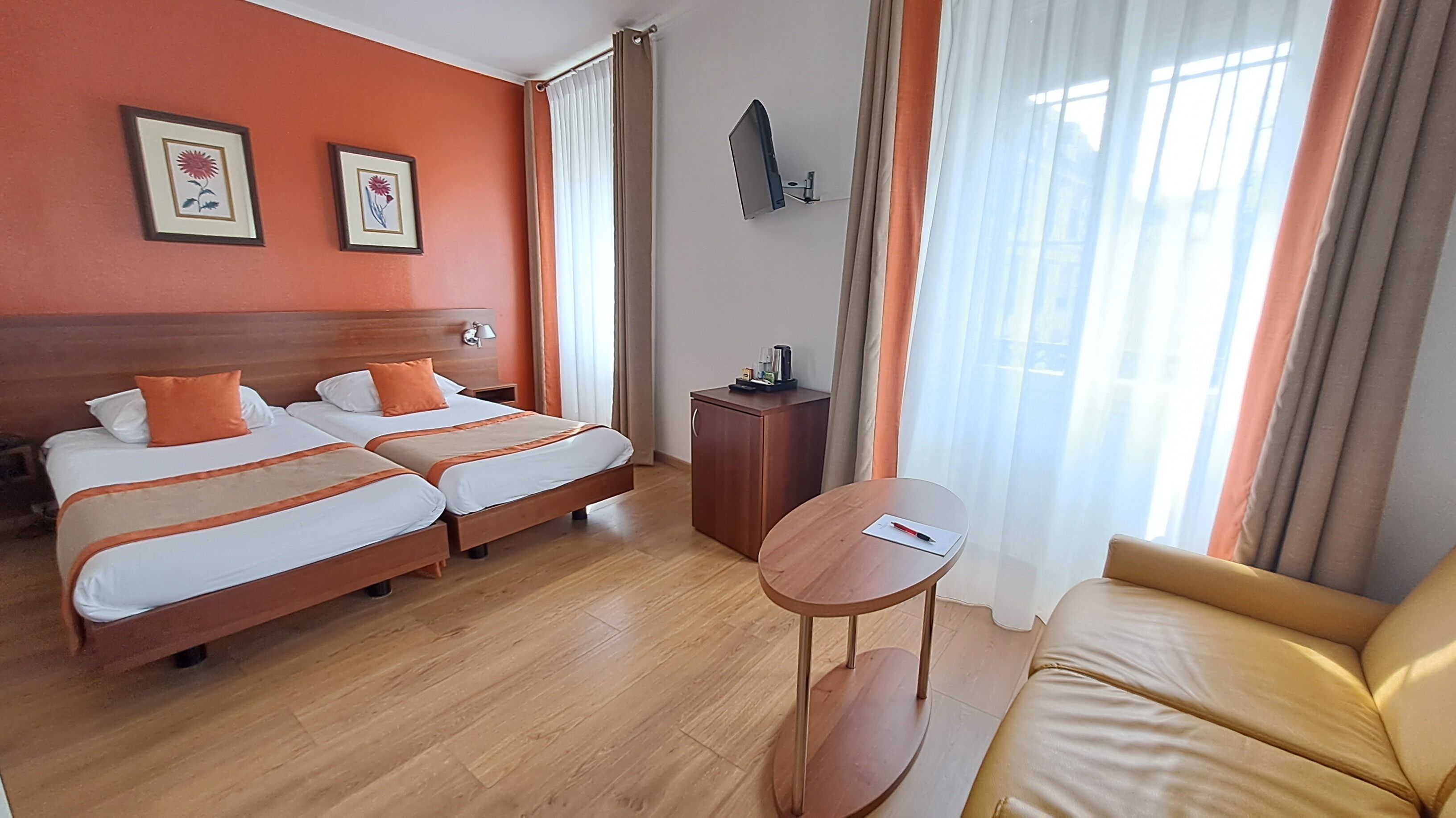 A hotel room with two beds, a sofa, a small table, and a TV mounted on the wall.