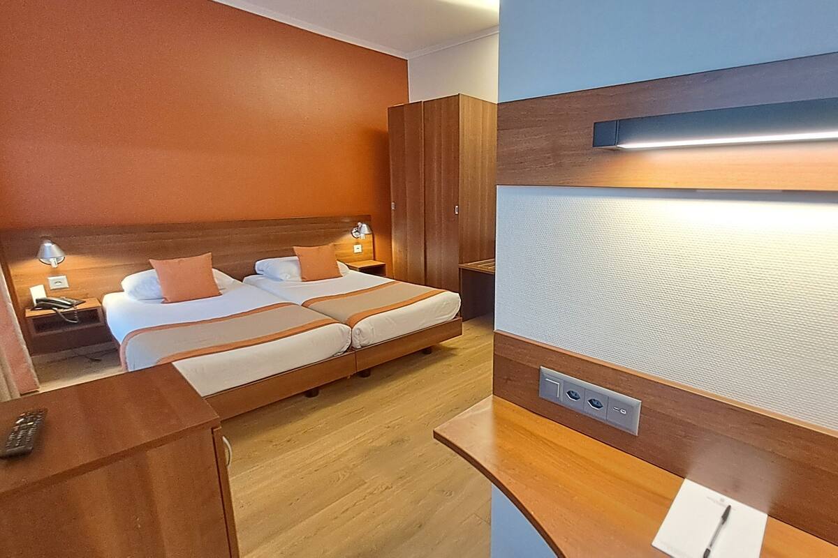 A hotel room with a double bed, a wooden headboard, a nightstand with a lamp, and a wall-mounted TV.