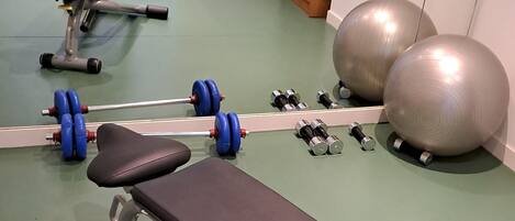 A gym with exercise equipment including a bench, dumbbells, and exercise balls.