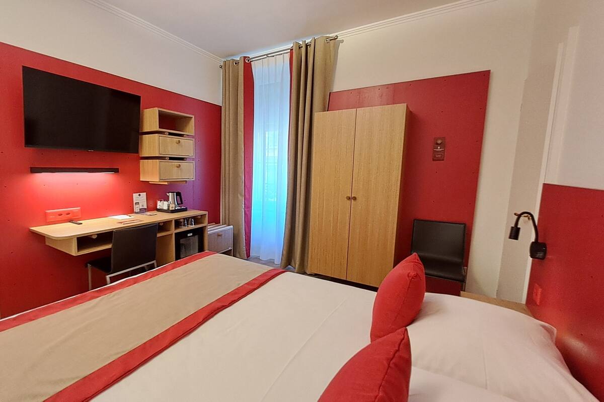 A hotel room with a bed, a desk, a wardrobe, and a TV mounted on the wall.