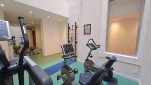 Une salle de sport équipée de machines de cardio, d’un porte-haltères fixé au mur et d’une grande fenêtre.