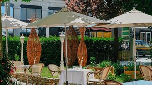 Un espace de restauration en plein air avec des chaises en osier et des tables blanches, protégé par des auvents à rayures.