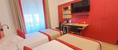 A hotel room with two beds, a desk with a computer, a TV, and a minibar.