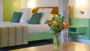 Une chambre d’hôtel avec un lit, des murs verts, une table de chevet et un vase rempli de fleurs.