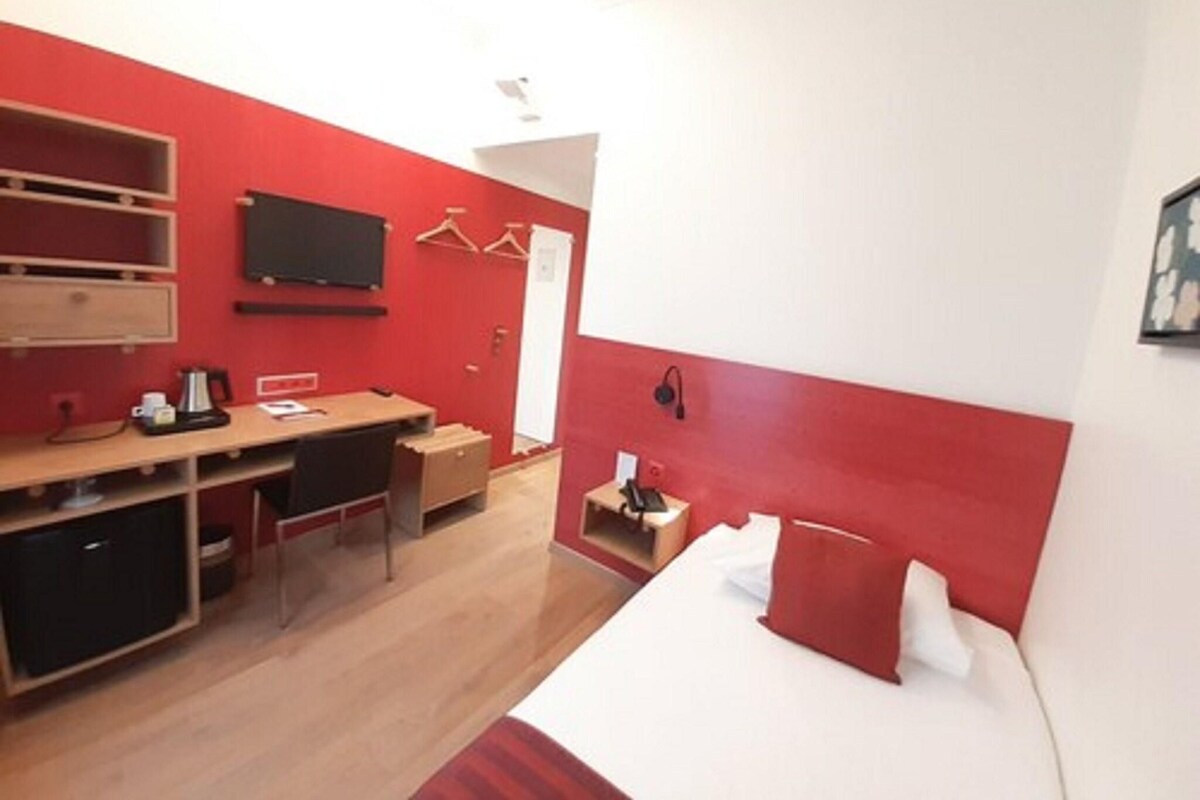 A hotel room with a bed, desk, chair, and a TV mounted on the wall.