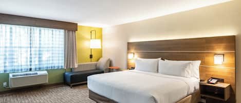 A hotel room with a large bed, a bedside table with a lamp, a small table, and a window with curtains.