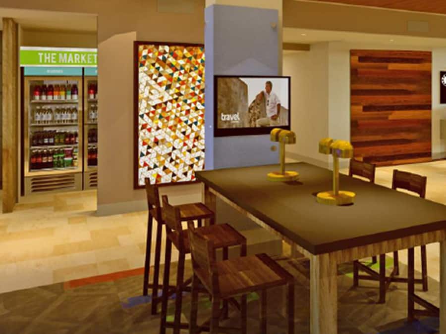 Un restaurant avec une longue table, des chaises, un écran de télévision et un mur orné d’un motif géométrique coloré.