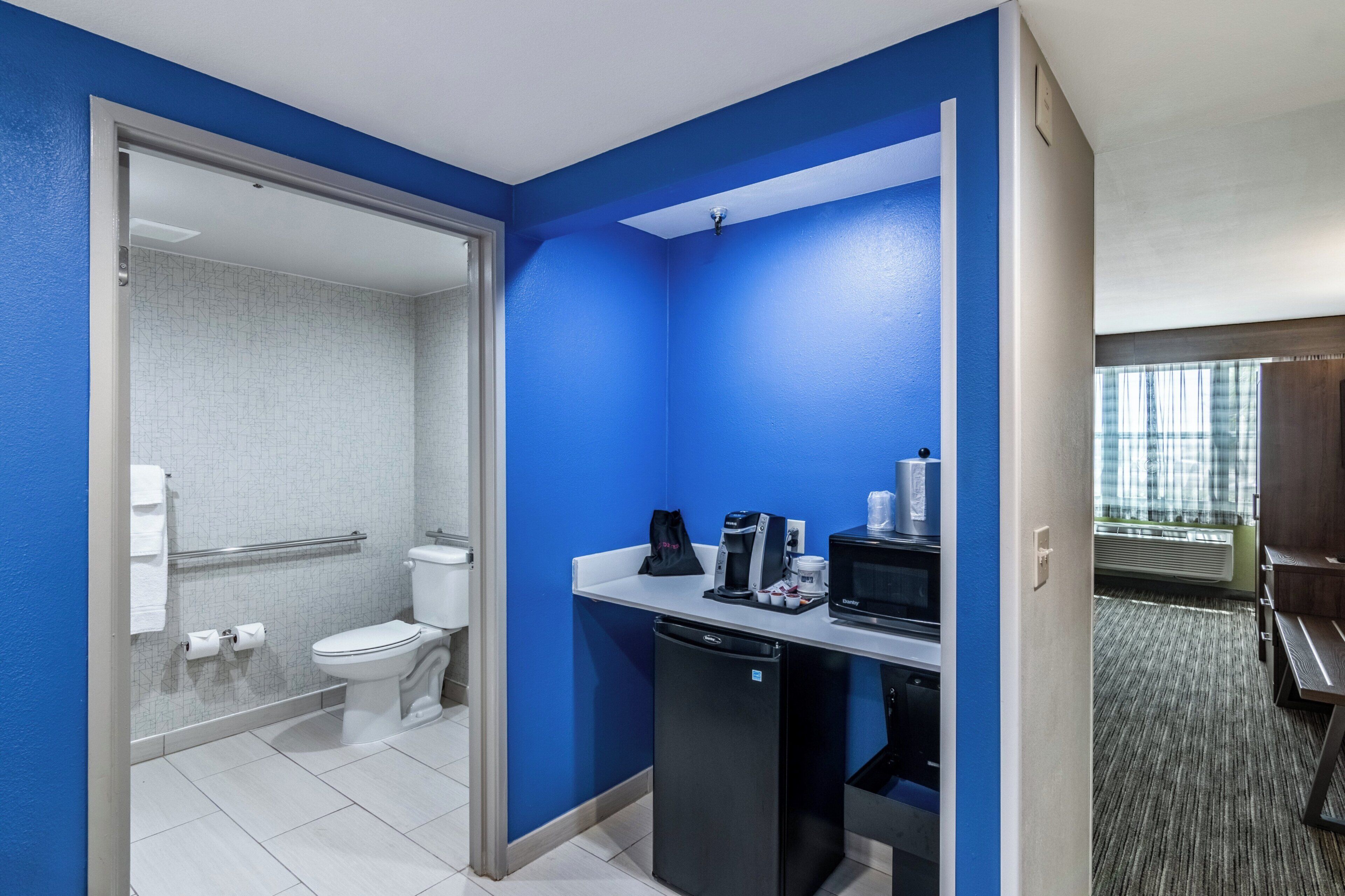 A hotel bathroom with a toilet, a shower, and a sink with a coffee maker.