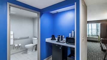 A hotel bathroom with a toilet, a shower, and a sink with a coffee maker.