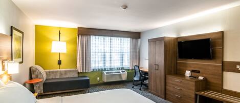 Habitación de hotel con una cama grande, un escritorio con silla, un televisor en la pared y una ventana con cortinas.