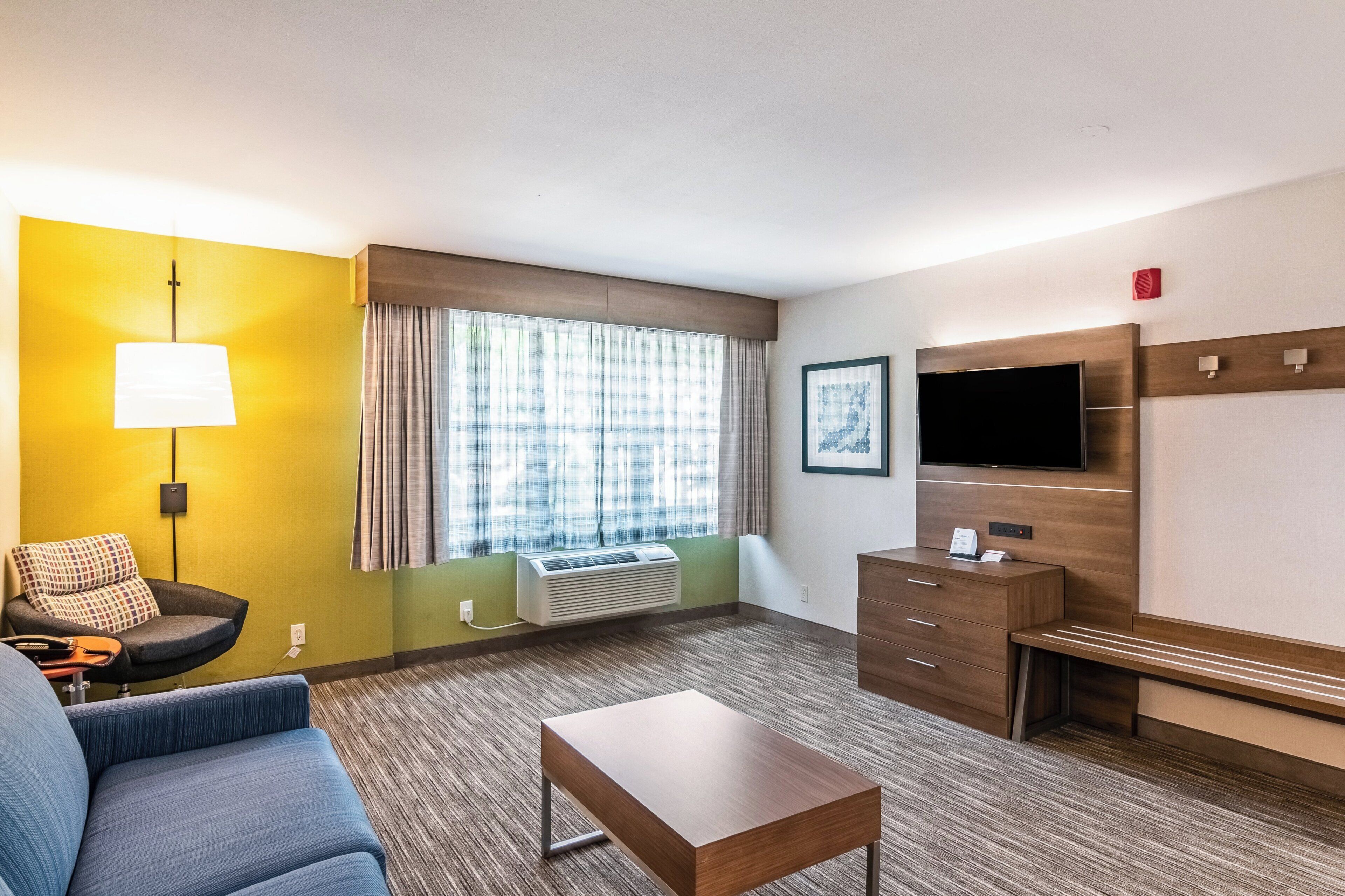 A hotel room with a sofa, a small table, a TV, a desk, and a window with curtains.