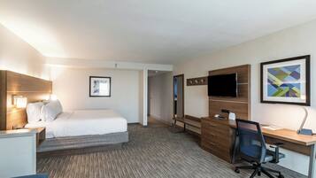 A hotel room with a bed, desk, chair, TV, and artwork.