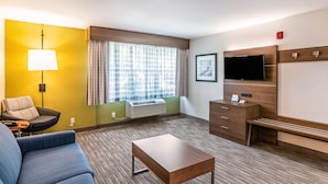 A hotel room with a sofa, a coffee table, a TV, a desk, and a window with curtains.
