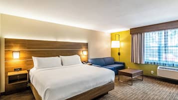 Habitación de hotel con una cama grande, un escritorio, un sofá, una lámpara y una ventana con cortinas.