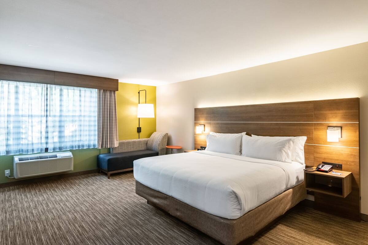 A hotel room with a large bed, bedside tables, a desk, a chair, a lamp, and a window with curtains.