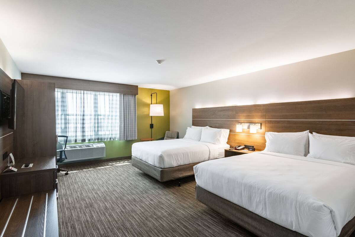 A hotel room with two beds, a desk, a lamp, and a view of the outdoors.