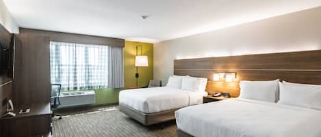 A hotel room with two beds, a desk, a lamp, and a view of the outdoors.