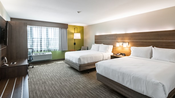 A hotel room with two beds, a desk, a lamp, and a view of the outdoors.