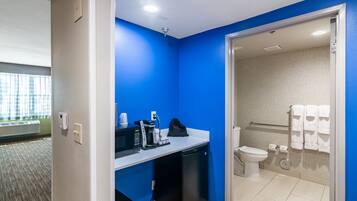 Een kleine badkamer met een blauwe accentmuur, een wastafel met een koffiezetapparaat, een zwarte koelkast en een toilet met een handdoekhouder.