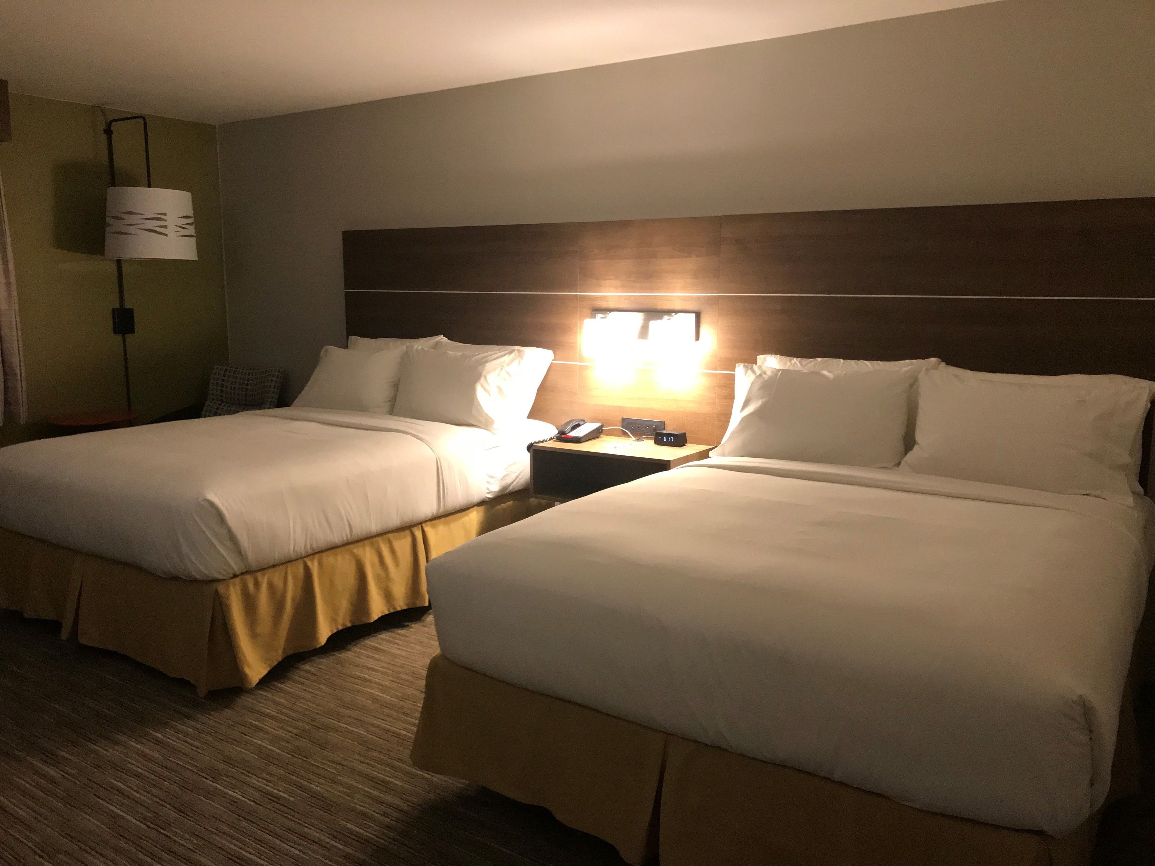 A hotel room with two beds, a nightstand with a lamp, and a wall-mounted light.