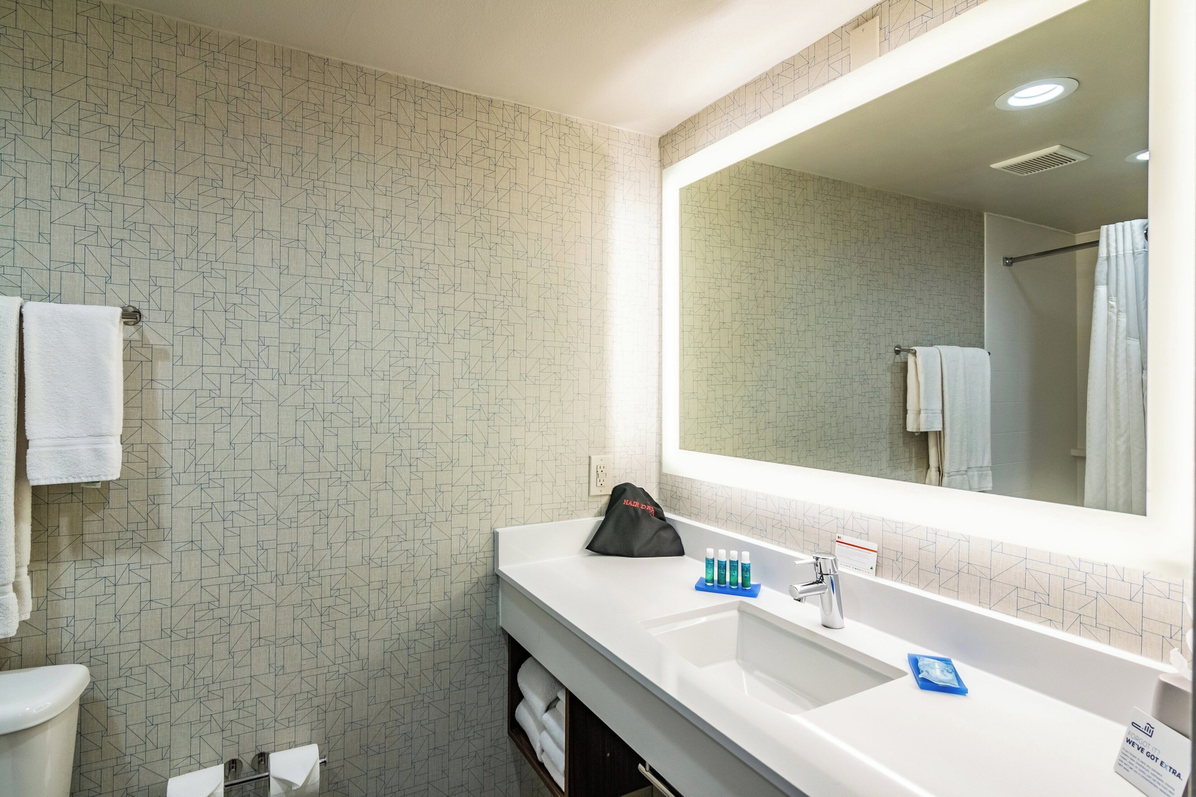 A bathroom with a geometric patterned wall, a white sink with a mirror above it, and a towel rack.