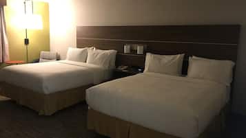A hotel room with two beds, a nightstand, a lamp, and a small table.