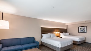 A hotel room with two beds, a sofa, a small table, and a wall-mounted lamp.