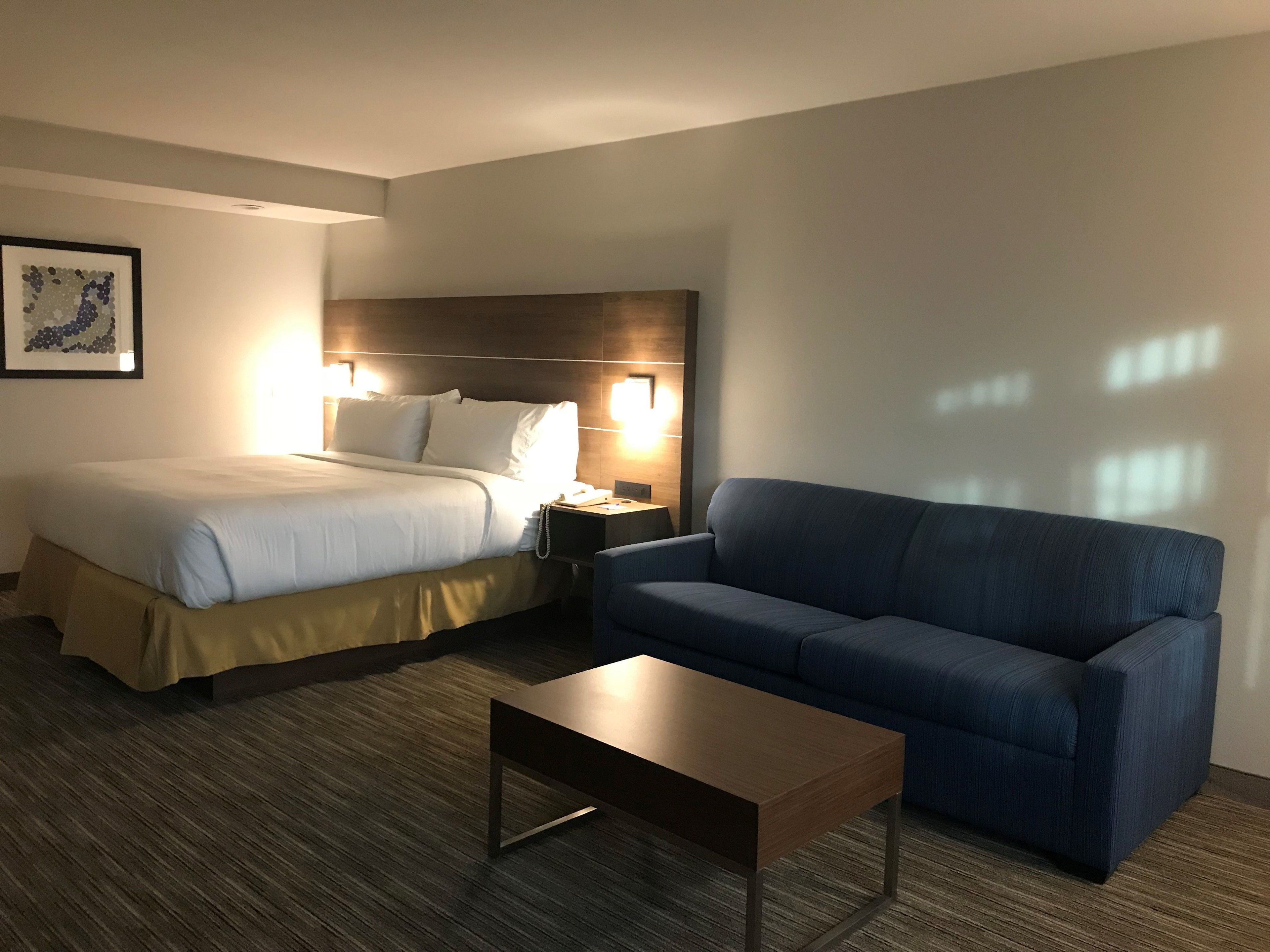 Quarto de hotel com cama, sofá, mesa de cabeceira e mesa de centro.