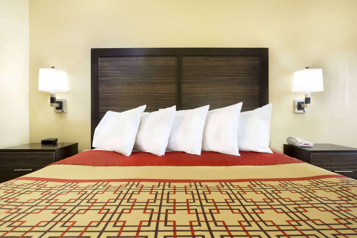 A hotel room with a large bed, a headboard, two bedside tables, a telephone, and a patterned throw blanket.