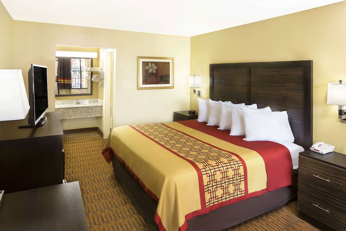 A hotel room with a bed, a desk, a television, and a bathroom visible through an open door.