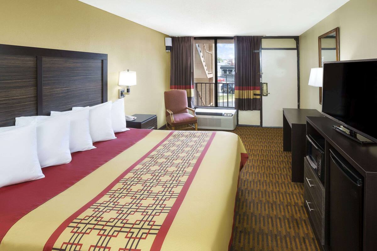 A hotel room with a large bed, a TV, a chair, and a desk.