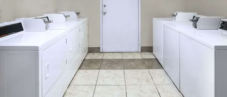 A laundry room with two rows of white washers and dryers, a tiled floor, and a closed door.