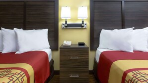 A hotel room with two beds, each with white bedding and red and yellow patterned bedspreads. There is a nightstand between the beds with a lamp and a phone. - Days Inn by Wyndham Columbus-North Fort Moore (Columbus)