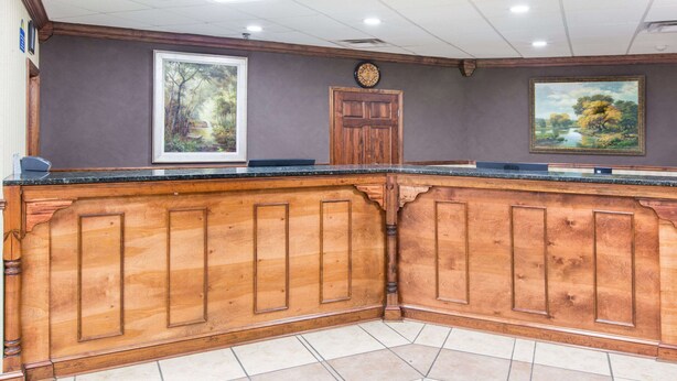 A reception area with a wooden reception desk, framed artwork on the walls, and a clock above the door. - Days Inn by Wyndham Columbus-North Fort Moore (Columbus)