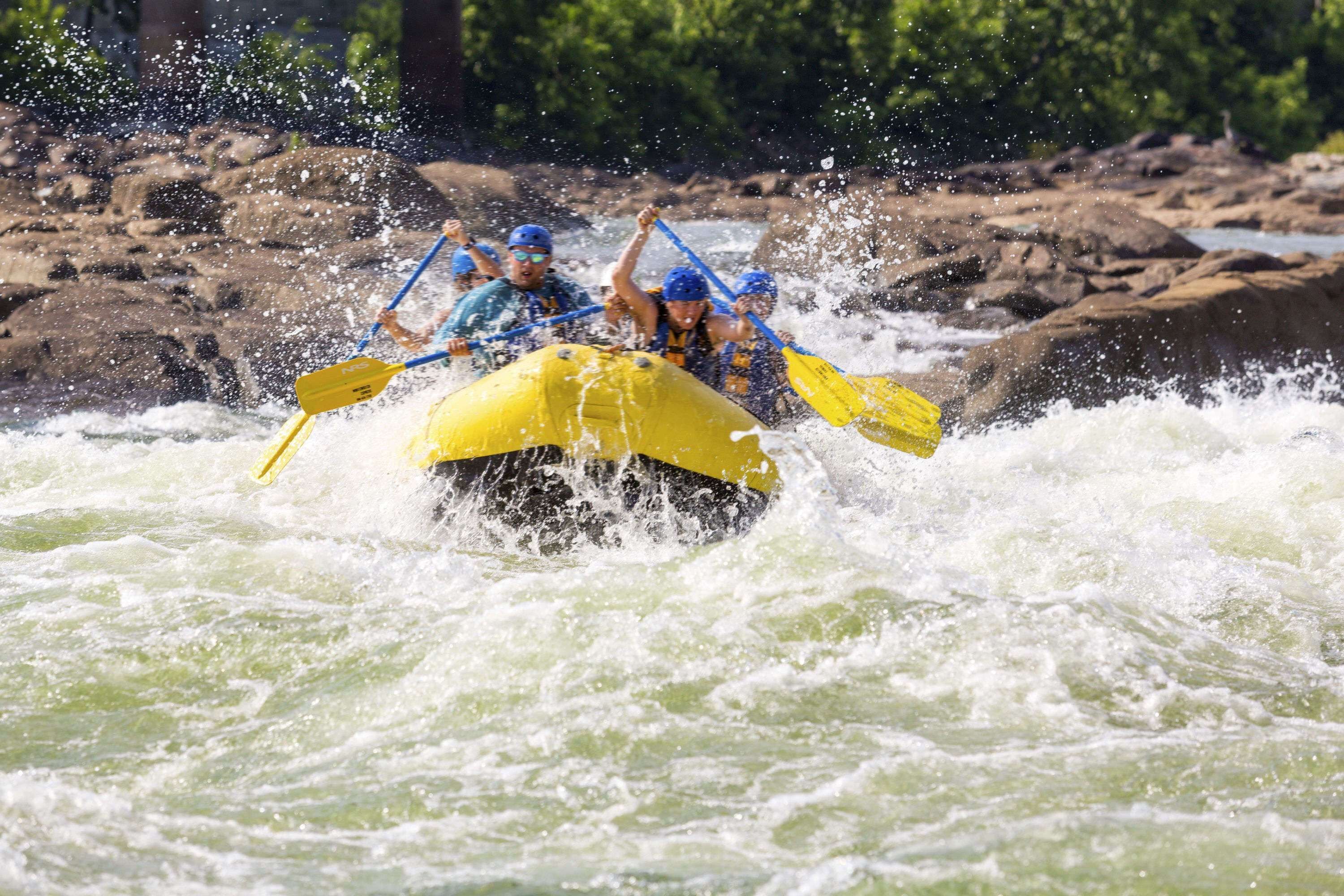A group of people in a yellow raft navigating through a river with rapids.