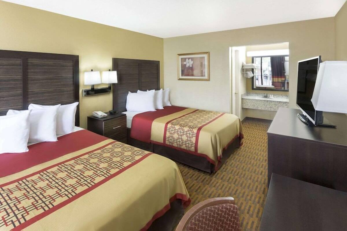 A hotel room with two beds, a desk, a TV, and a bathroom visible through an open door.