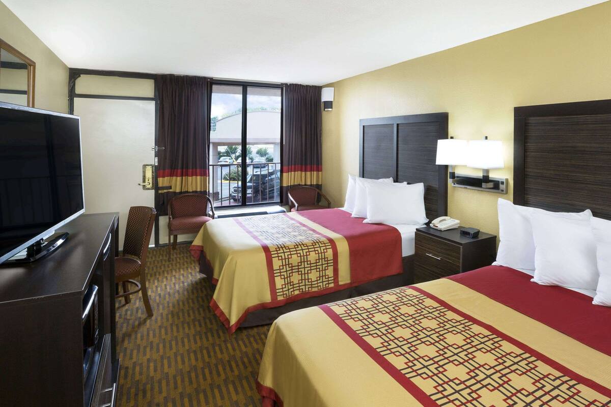 A hotel room with two beds, a TV, a desk, and a balcony with a view.