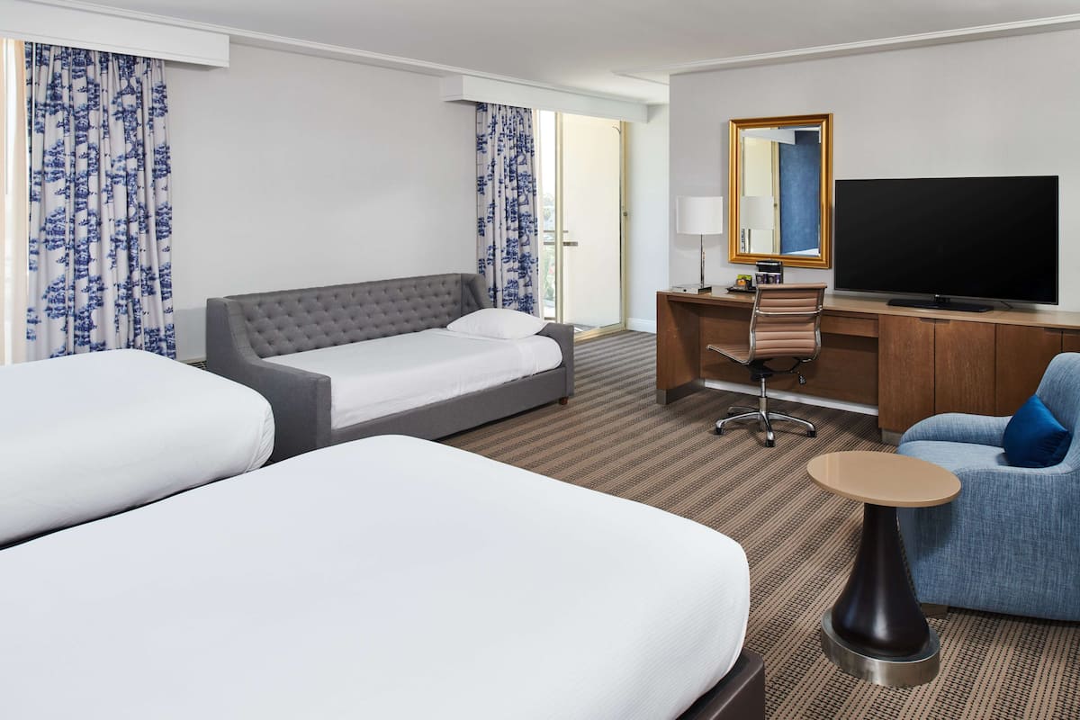 A hotel room with two beds, a desk, a chair, a television, and a large mirror.