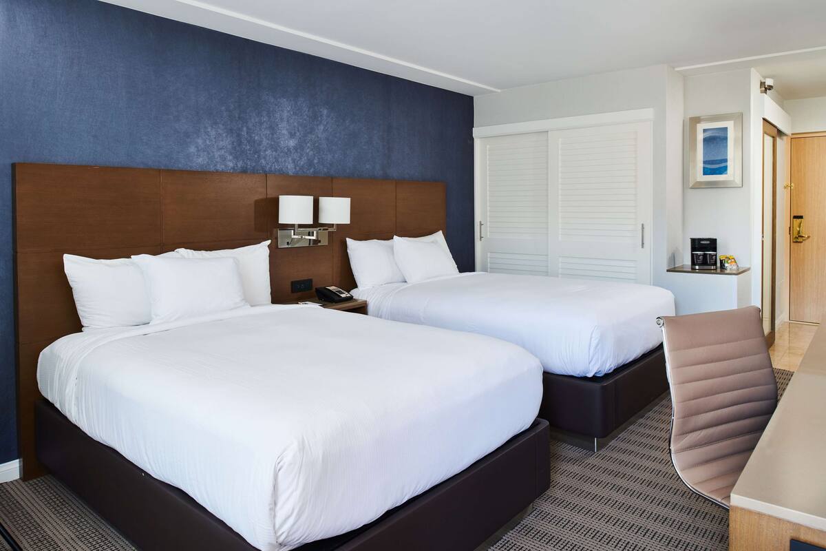 A hotel room with two beds, a desk, a chair, and a nightstand with a phone.