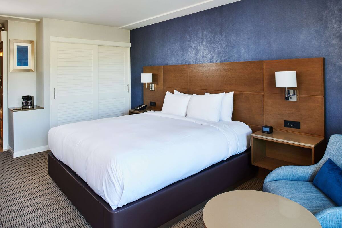 A hotel room with a large bed, bedside tables, a chair, and a small table.
