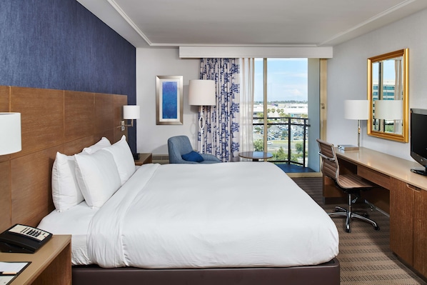 Une chambre d’hôtel avec un grand lit, un bureau, une chaise, une télévision et une vue sur la ville.